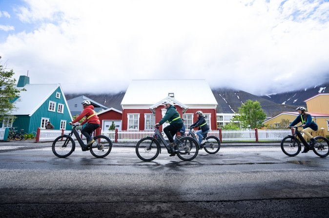Cyclists passing the painted timber houses of Ísafjörður in the rain