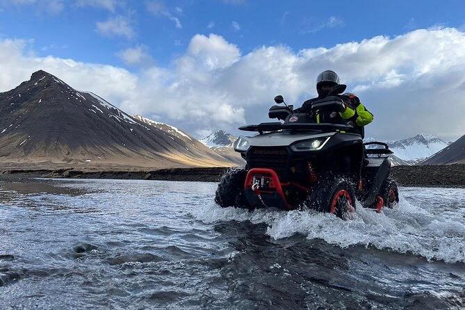 A quad bike crossing a shallow river below a Westfjords peak