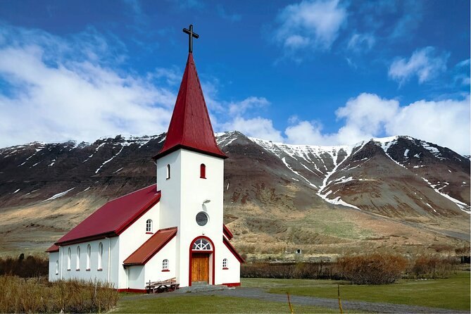 A white church with a red roof below snow-streaked Westfjords mountains